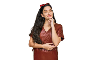 Wall Mural - Brunette young woman wearing dress and sunglasses looking confident at the camera with smile with crossed arms and hand raised on chin. thinking positive.