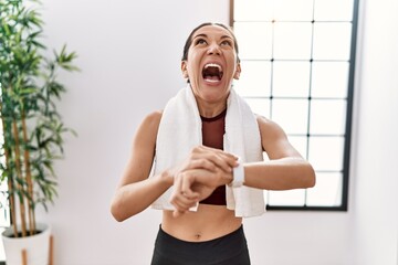 Poster - Young hispanic woman wearing sportswear looking stopwatch at sport center angry and mad screaming frustrated and furious, shouting with anger looking up.