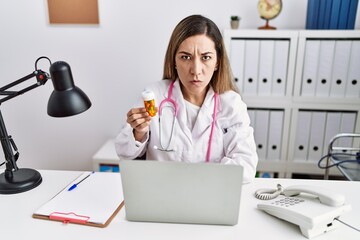 Canvas Print - Young hispanic woman wearing doctor uniform holding pills at the clinic skeptic and nervous, frowning upset because of problem. negative person.