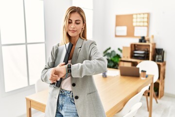 Blonde business woman at the office checking the time on wrist watch, relaxed and confident