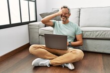 Middle Age Hispanic Man Using Laptop Sitting On The Floor At The Living Room Smiling And Laughing With Hand On Face Covering Eyes For Surprise. Blind Concept.