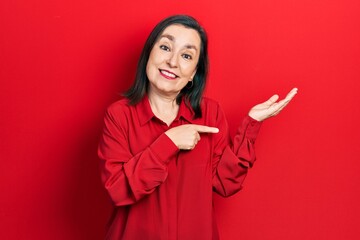 Sticker - Middle age hispanic woman wearing casual clothes amazed and smiling to the camera while presenting with hand and pointing with finger.