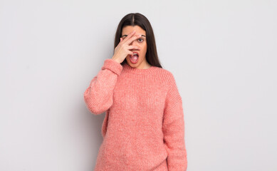 Wall Mural - pretty young woman looking shocked, scared or terrified, covering face with hand and peeking between fingers