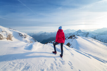 Wall Mural - young woman in red jacket in snowy mountains at sunset in winter. landscape with beautiful girl on t