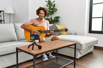 Canvas Print - Young hispanic man recording with camera playing classical guitar at home.