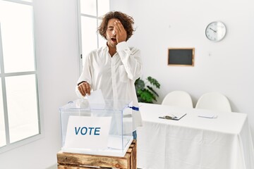 Sticker - Young hispanic man voting putting envelop in ballot box yawning tired covering half face, eye and mouth with hand. face hurts in pain.