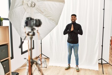 Poster - Young hispanic man with beard posing as model at photography studio praying with hands together asking for forgiveness smiling confident.