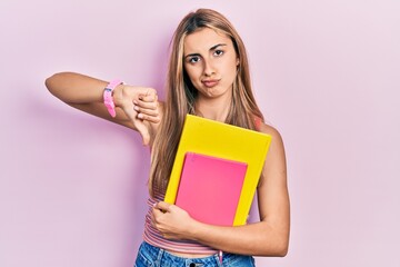 Poster - Beautiful hispanic woman holding books with angry face, negative sign showing dislike with thumbs down, rejection concept