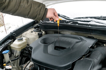 Close-up side view of auto mechanic man checking engine oil level in car, workshop, garage. car repairing service with open hood,outside backyard in winter