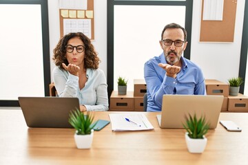 Poster - Middle age hispanic woman and man sitting with laptop at the office looking at the camera blowing a kiss with hand on air being lovely and sexy. love expression.