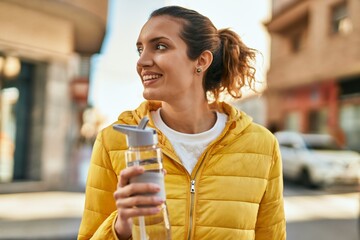 Young hispanic girl smiling happy drinking bottle of water at the city.