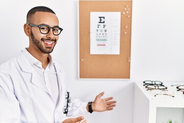 Wall Mural - African american optician man standing by eyesight test inviting to enter smiling natural with open hand