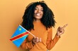 African american woman with afro hair holding democratic republic of the congo flag smiling happy pointing with hand and finger to the side