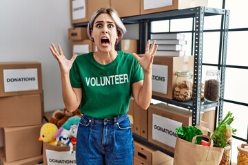 Sticker - Young beautiful woman wearing volunteer t shirt at donations stand crazy and mad shouting and yelling with aggressive expression and arms raised. frustration concept.