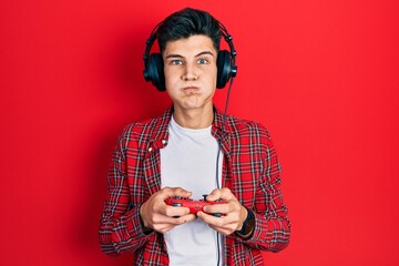 Sticker - Young hispanic man playing video game holding controller puffing cheeks with funny face. mouth inflated with air, catching air.