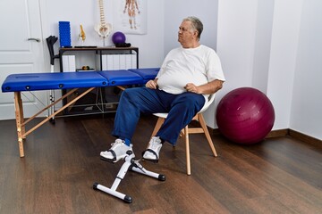 Canvas Print - Senior caucasian man at physiotherapy clinic using pedal exerciser looking to side, relax profile pose with natural face with confident smile.