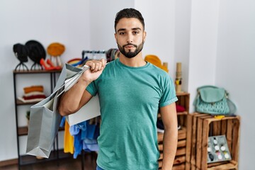 Poster - Young handsome man with beard holding shopping bags at retail shop relaxed with serious expression on face. simple and natural looking at the camera.