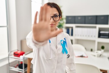 Wall Mural - Young brunette doctor woman wearing stethoscope at the clinic doing stop sing with palm of the hand. warning expression with negative and serious gesture on the face.