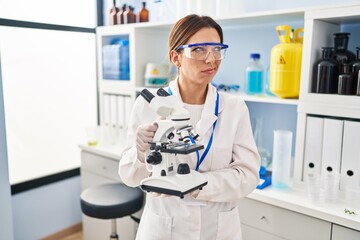 Sticker - Young brunette woman working at scientist laboratory with microscope smiling looking to the side and staring away thinking.