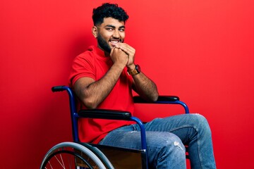 Wall Mural - Arab man with beard sitting on wheelchair laughing nervous and excited with hands on chin looking to the side