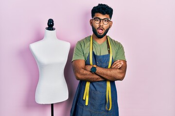 Canvas Print - Arab man with beard dressmaker designer wearing atelier apron afraid and shocked with surprise and amazed expression, fear and excited face.