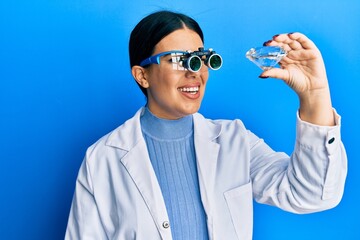 Canvas Print - Beautiful brunette jeweller woman holding brilliant diamond stone wearing magnifier glasses winking looking at the camera with sexy expression, cheerful and happy face.