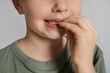 Little girl biting her nails on grey background, closeup