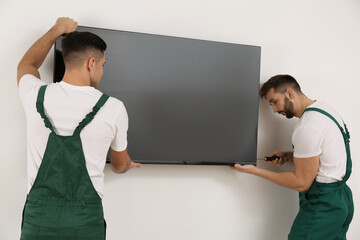 Canvas Print - Professional technicians with screwdriver installing modern flat screen TV on wall indoors