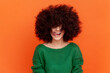 © khosrork - Happy positive woman with Afro hairstyle wearing green casual style sweater showing tongue out, demonstrating her hair, need cutting bangs. Indoor studio shot isolated on orange background.