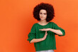 Young adult woman with Afro hairstyle wearing green casual style sweater showing time out hand gesture, looking at camera, worried about deadline. Indoor studio shot isolated on orange background.