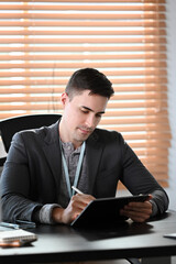 Wall Mural - Portrait of handsome businessman sitting at office desk and using digital tablet.