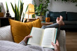 © Daniel - POV of young woman relaxing at home reading a book lying on sofa.