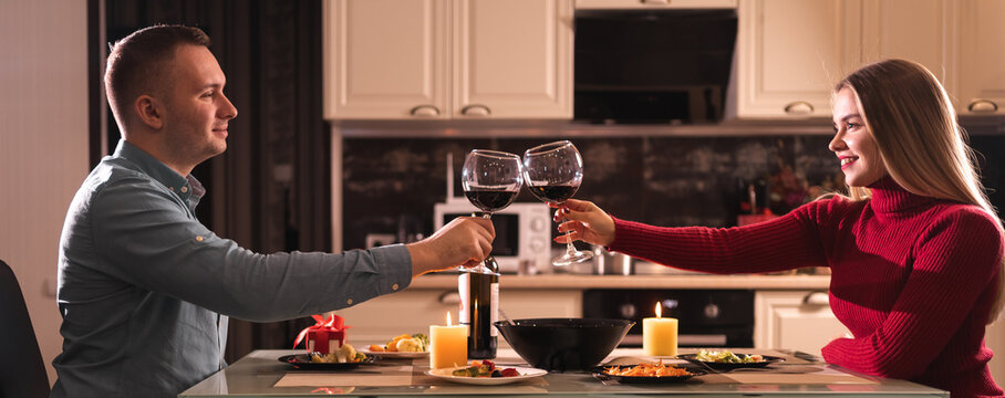 A couple in love on valentine's day have dinner at home and drink red wine in glasses. Alcohol at dinner for two. Date of a man and a woman.