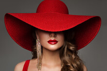Fashion Woman In Hat With Red Lips Make Up And Golden Earring. Beauty Model Face Hidden By Wide Broad Brim Hat. Elegant Lady Close Up Portrait Over Gray