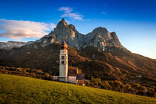Seis Am Schlern, Italy - The Famous St. Valentin Church And Mount Sciliar Mountain At Sunset. Idyllic Mountain Scenery In The Italian Dolomites With Blue Sky And And Warm Sunlight At South Tyrol