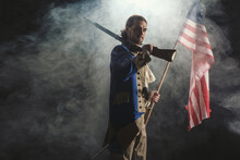 American Revolution War Soldier With Flag Of Colonies And Musket Gun Over Dramatic Smoke Background. 4 July Independence Day Of USA Concept Photo Composition: Soldier And Flag.