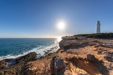 Australia, Victoria, Sun Shining Over Rough Coast Of Cape Nelson State Park With Cape Nelson Lighthouse In Background