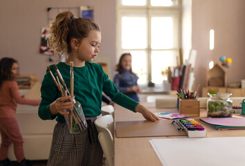 Wall Mural - Happy little girl with her friends preparing for art and craft class indoors at school