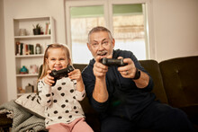 Grandfather And Granddaughter Playing Video Game Together At Home