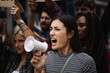 Young woman manifesting marching on a protest shouting into a megaphone