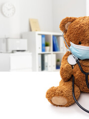 Wall Mural - medicine, healthcare and pandemic concept - teddy bear toy in protective mask with stethoscope over medical office at hospital background