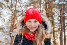 Portrait Of A Charming Little Girl In A Red Hat In A Snowy Forest In Winter. Christmas Winter Holidays. Happy Childhood