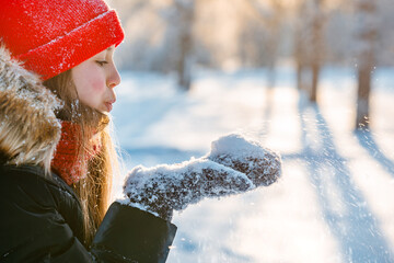 Wall Mural - Beautiful little girl blowing snowflakes in white winter forest covered with snow