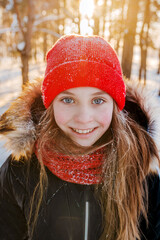 Wall Mural - Portrait of a charming little girl in a red hat in a snowy forest in winter. Christmas winter holidays. Happy childhood