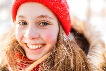 Wall Mural - Portrait of a charming little girl in a red hat in a snowy forest in winter. Christmas winter holidays. Happy childhood