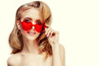 © Miramiska - Beautiful girl in red plastic glasses in the shape of a heart. Woman on February 14th, Valentine's Day. A model with amazing makeup and hair.
