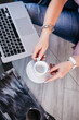 © NADIN - Woman holding cup of coffee and working with laptop