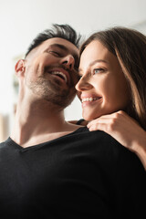 Wall Mural - low angle view of happy young woman embracing laughing boyfriend in bedroom.