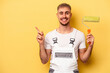Young painter man isolated on yellow background smiling and pointing aside, showing something at blank space.