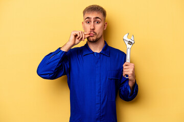 Wall Mural - Young electrician caucasian man isolated on yellow background with fingers on lips keeping a secret.